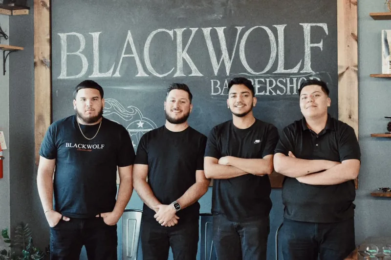 Four men in black shirts in front of the Blackwolf Barbershop chalkboard